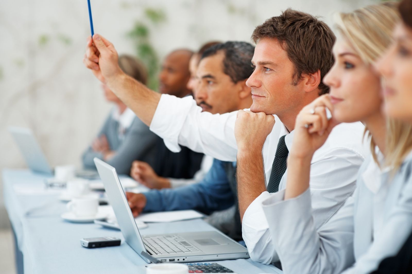 Man raising his hand while holding a pencil in his hand in a meeting